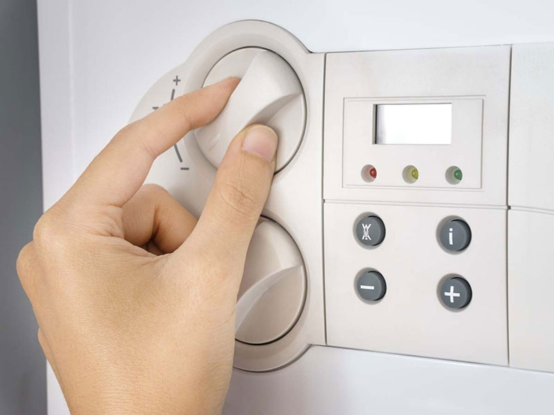 A person's hand adjusting a central heating boiler control