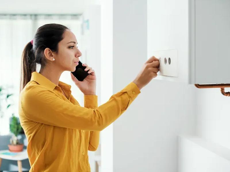 Woman on the phone while adjusting her central heating system controls
